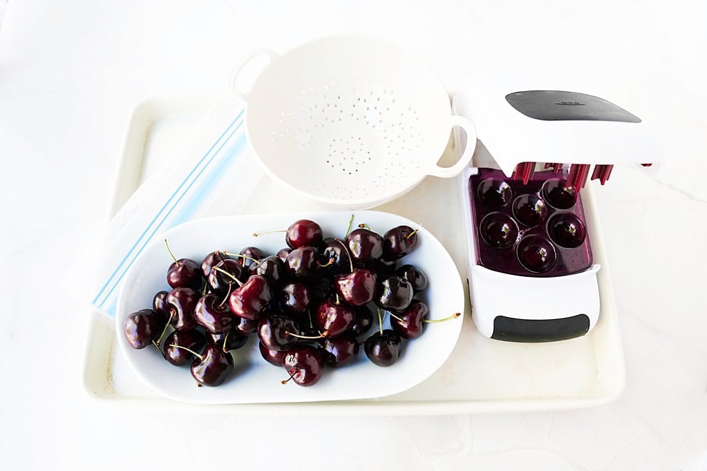 cherries on a plate with a bowl and a pitter