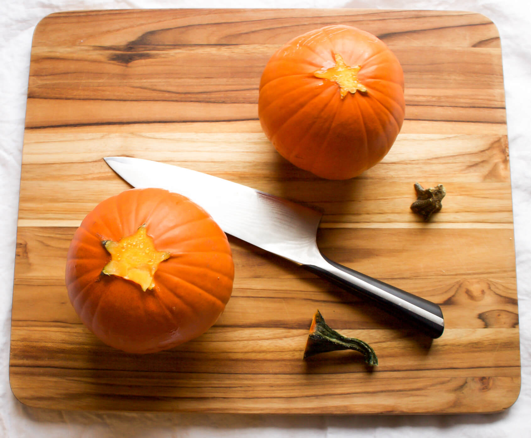 small baking pumpkins on cutting board with stems removed
