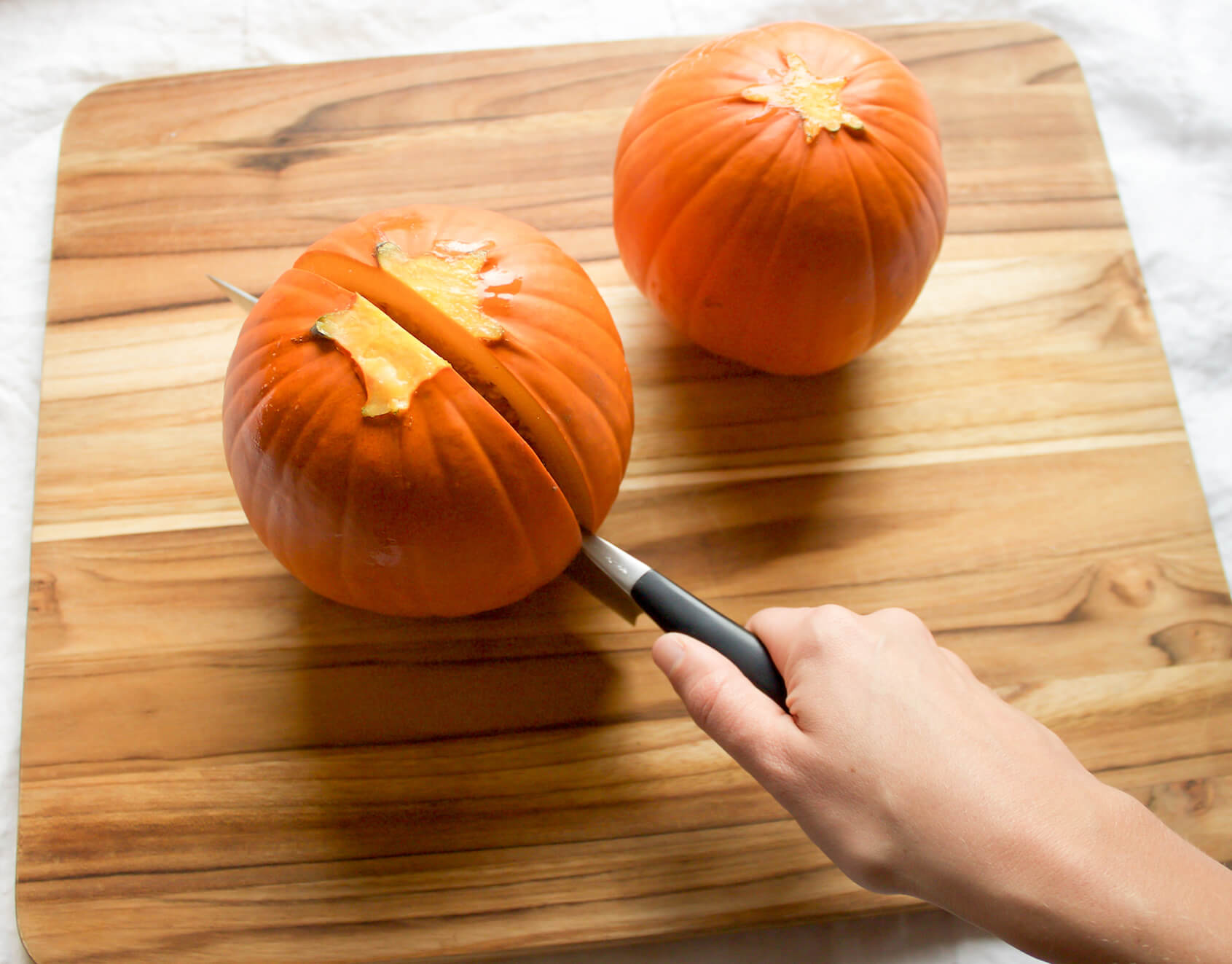 small baking pumpkins on cutting board with hand using a knife to cut