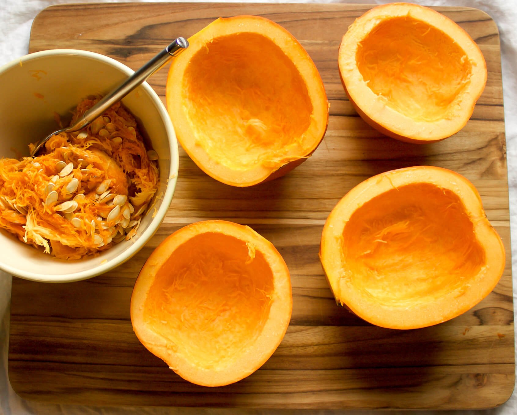 small baking pumpkins on cutting board with seeds removed in a bowl