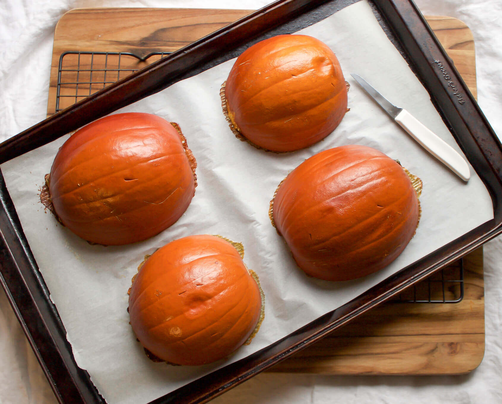 small baking pumpkins on baking sheet with parchment paper after being baked in the oven with pairing knife