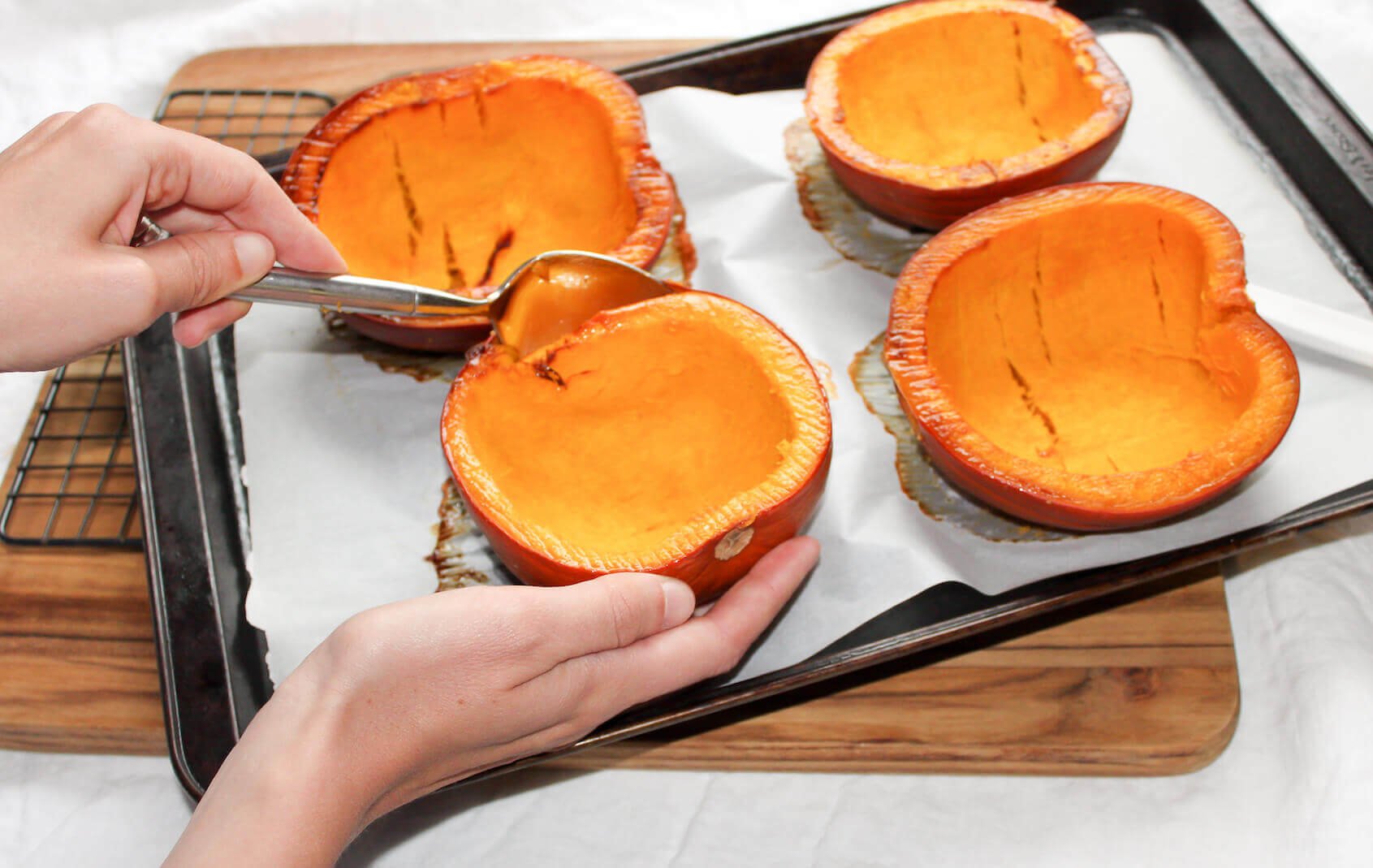hand using spoon to remove the pumpkin from a cooked pumpkin on a baking sheet
