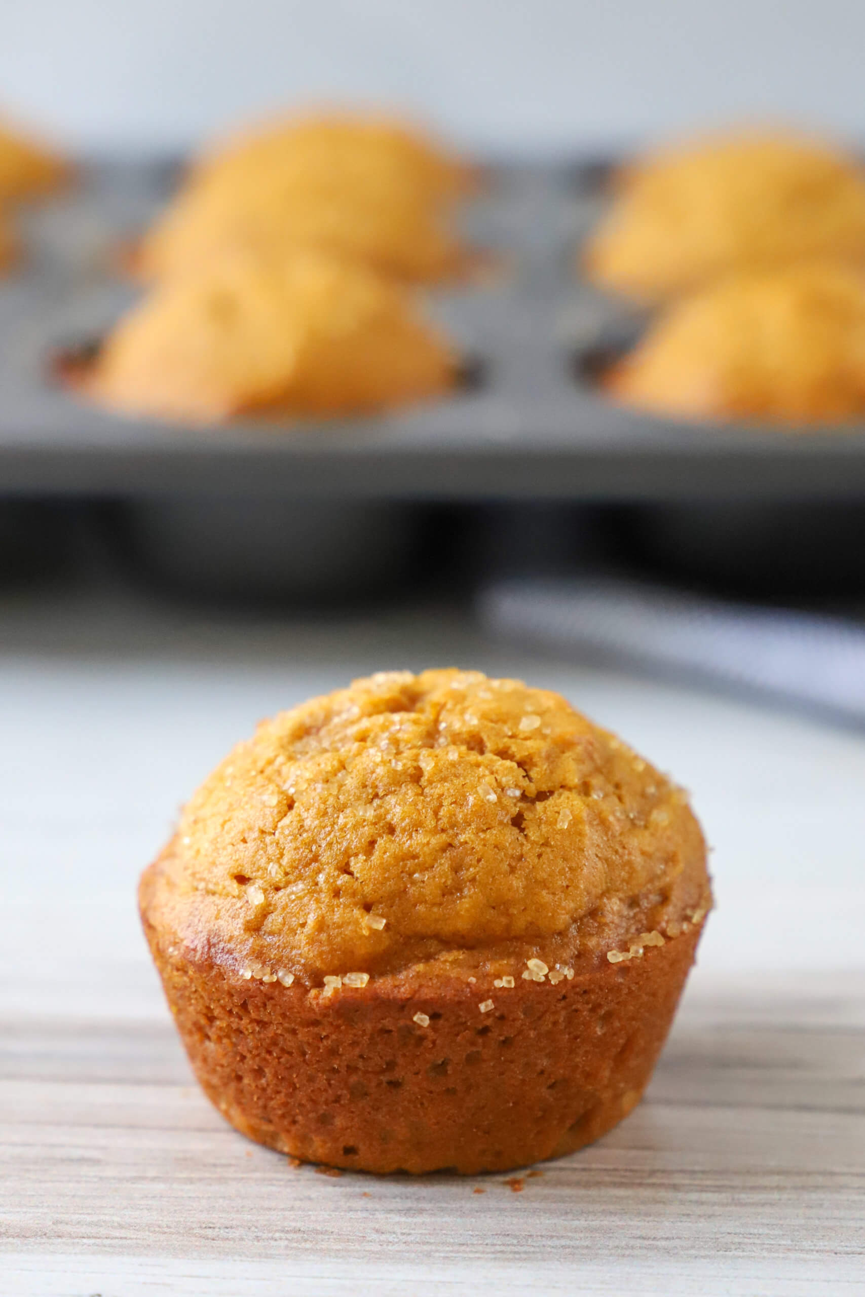 pumpkin muffin on table with muffin tin with pumpkin muffins