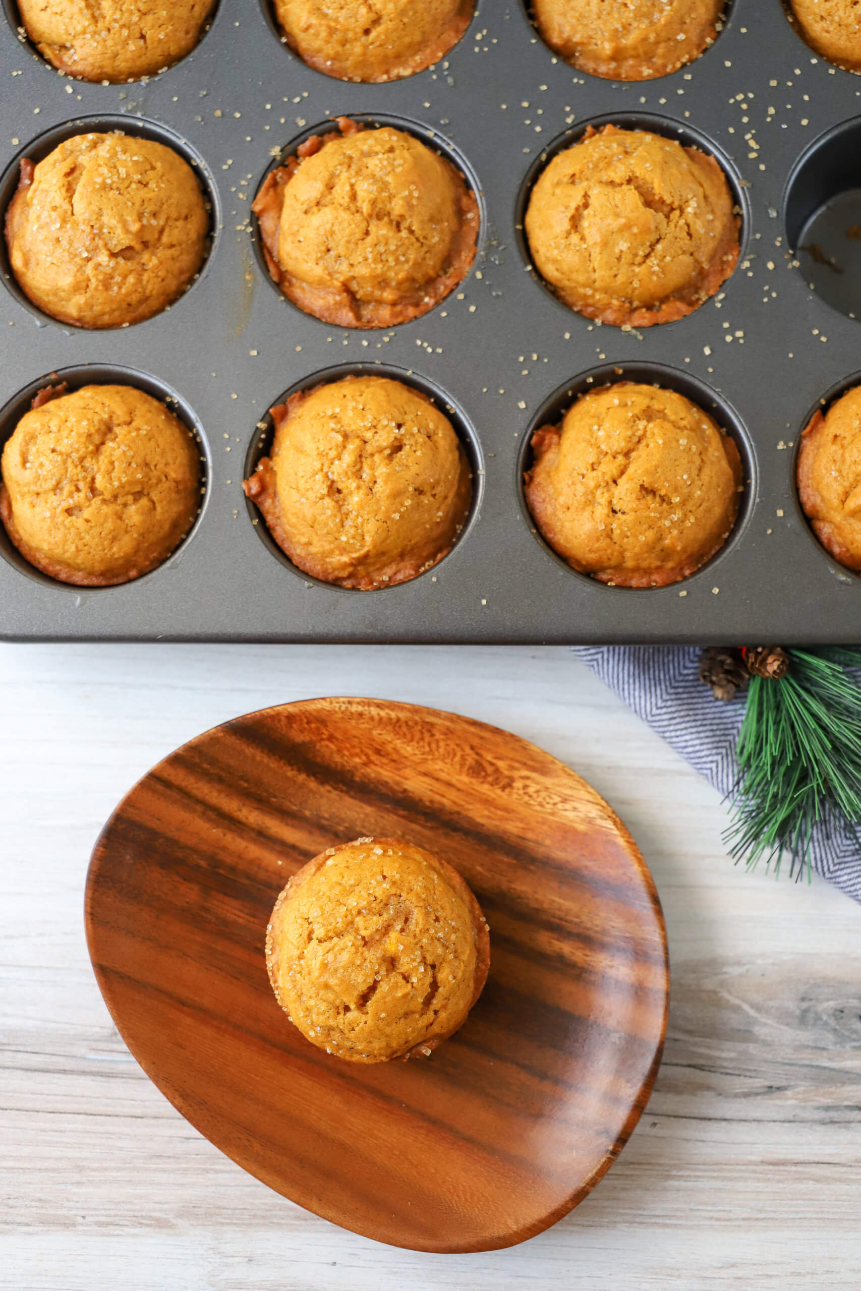 overhead vertical shot of pumpkin muffin on a plate with pumpkin muffins in muffin pan