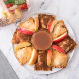 horizontal overhead shot of air fryer apple hand pies on a white plate with caramel sauce for dipping and sliced apples