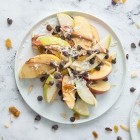 vertical shot of apple and pear nachos on a white plate with sliced almonds, golden raisins and chocolate chips
