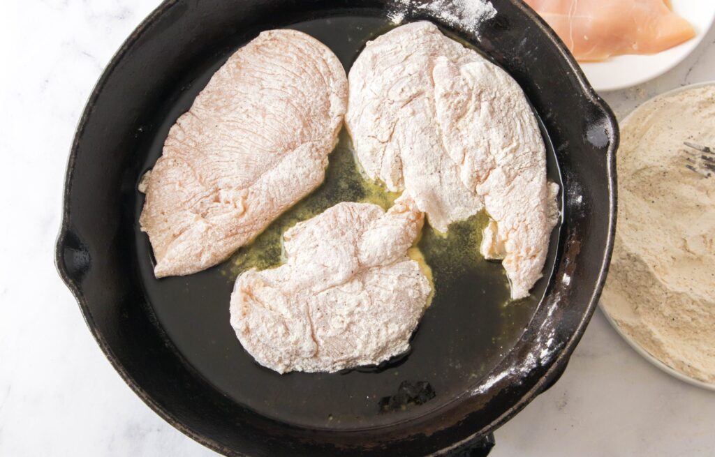 3 flour covered chicken breasts in a skillet