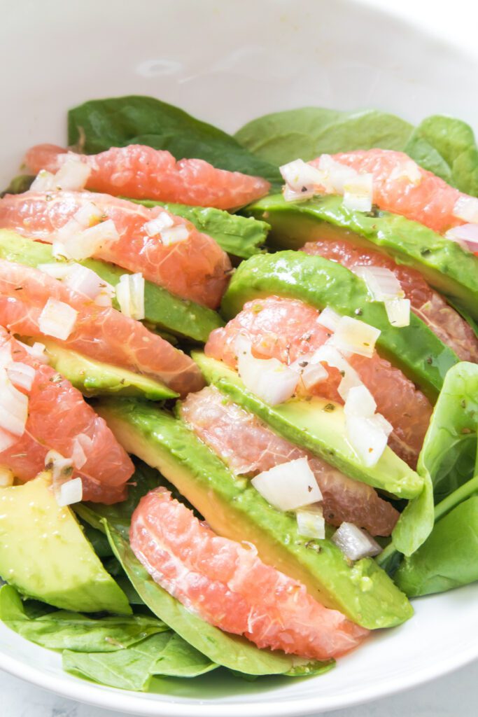 close up vertical shot of grapefruit avocado salad over spinach in white bowl