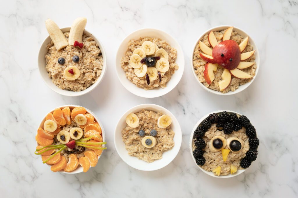 6 bowls of oatmeal with animals made from fruit