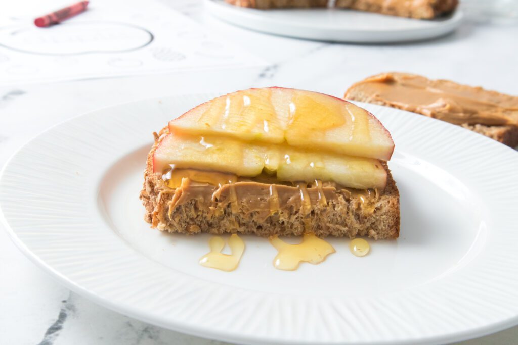 apple and honey on peanut butter bread on a white plate