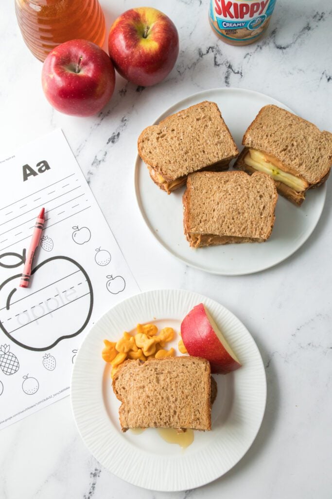 apple, peanut butter and honey sandwich on a white plate with school work