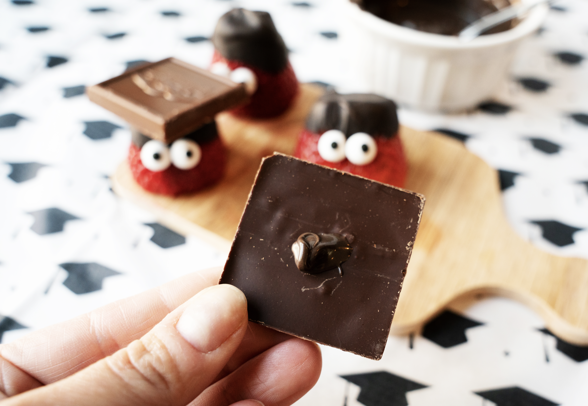 Melted chocolate dot on chocolate square with graduation strawberries in the background