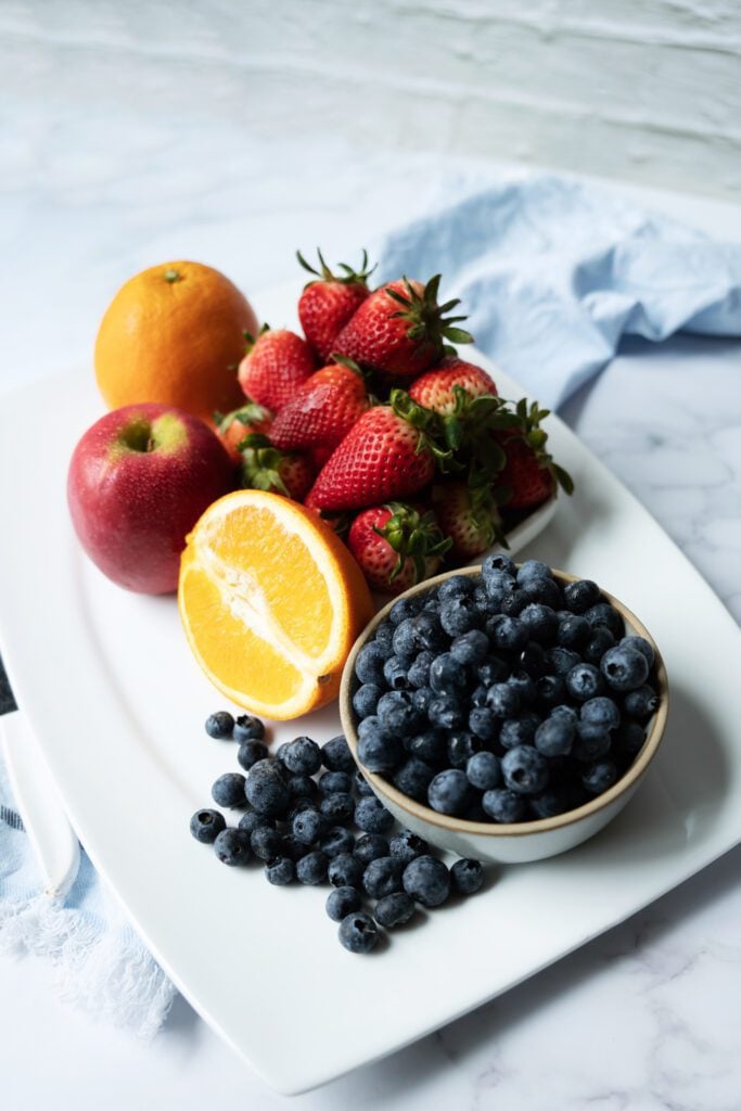 fruit on a plate: blueberries, strawberries, oranges, apple