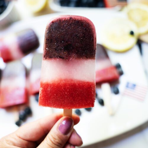 hand holding fruit popsicle with popsicles in the background on white serving tray