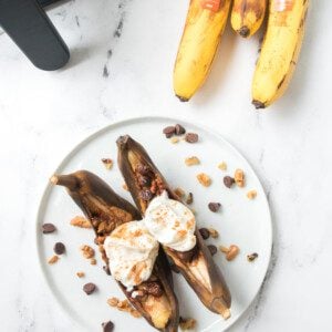 air fryer banana split on white plate with bananas and air fryer in background