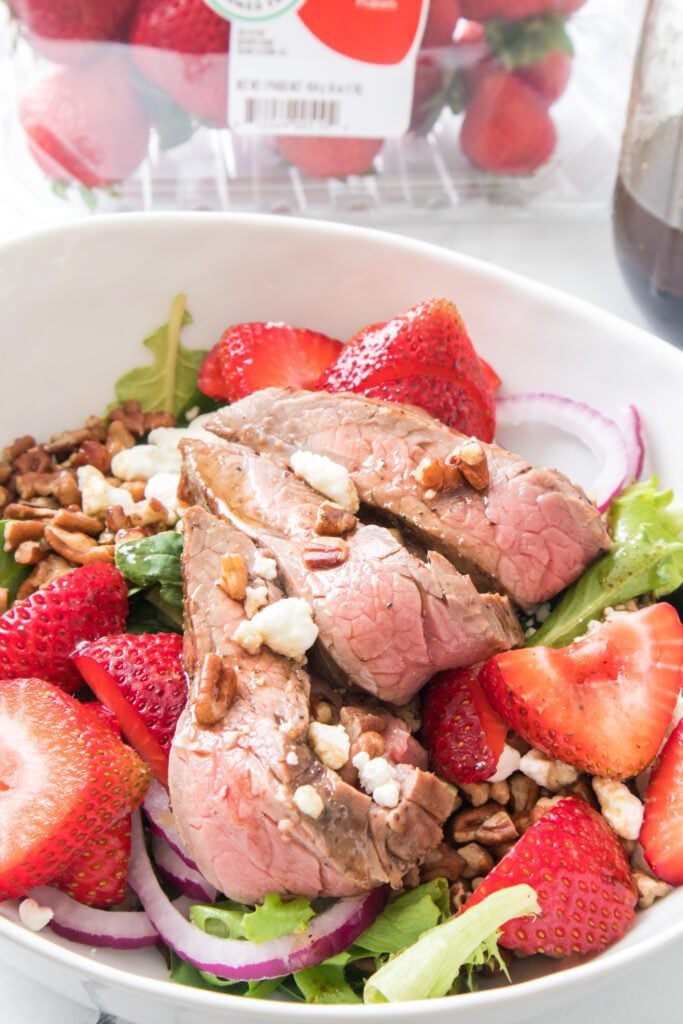 close up shot of steak and strawberry salad in white bowl