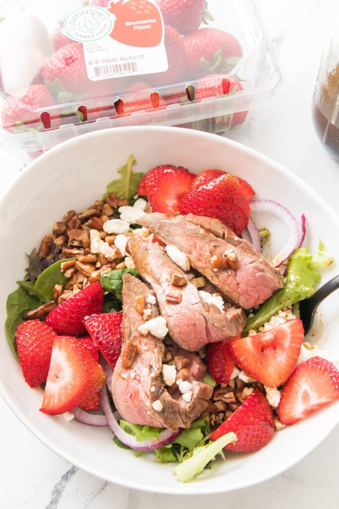 vertical image of strawberry salad with naturipe strawberries in background