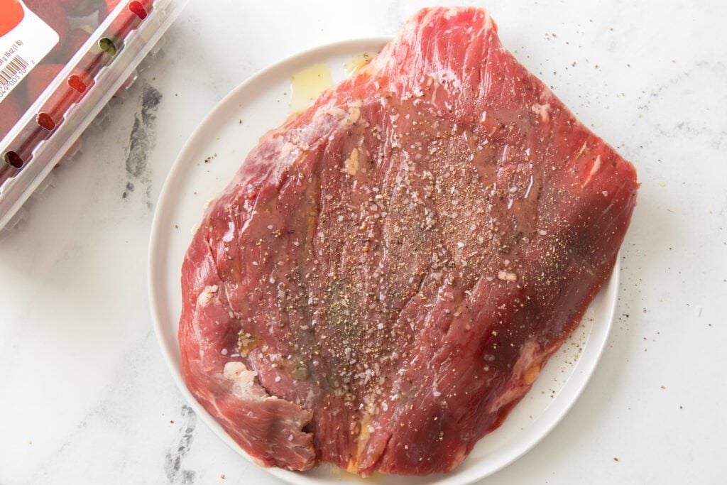 flank steak on a white plate with olive oil, kosher salt and black pepper