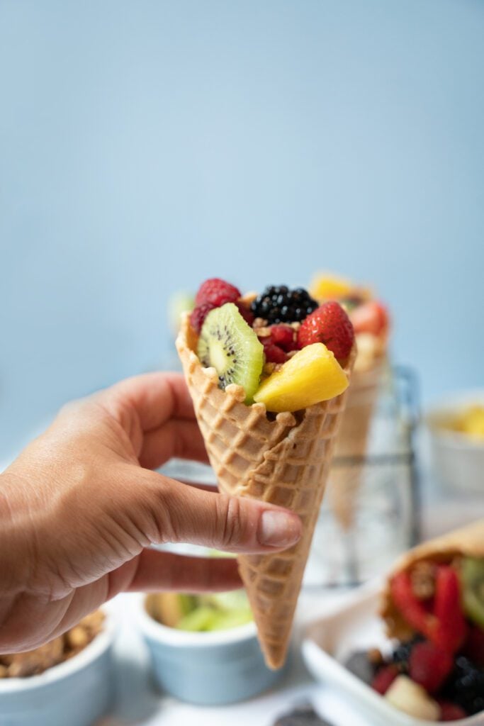 Hand holding ice cream cone fruit salad