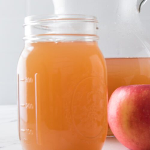 vertical shot of homemade apple cider in mason jar with pitcher in background