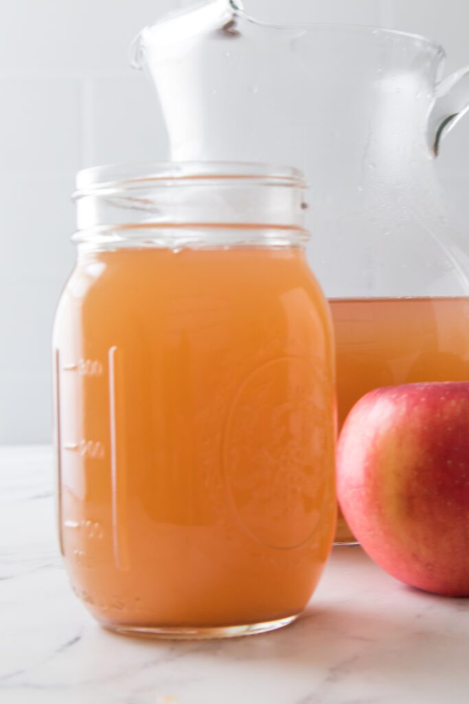 vertical shot of homemade apple cider in mason jar with pitcher in background