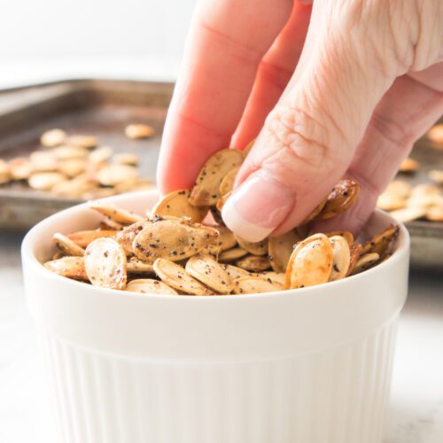 hand picking up roasted pumpkin seeds in white dish