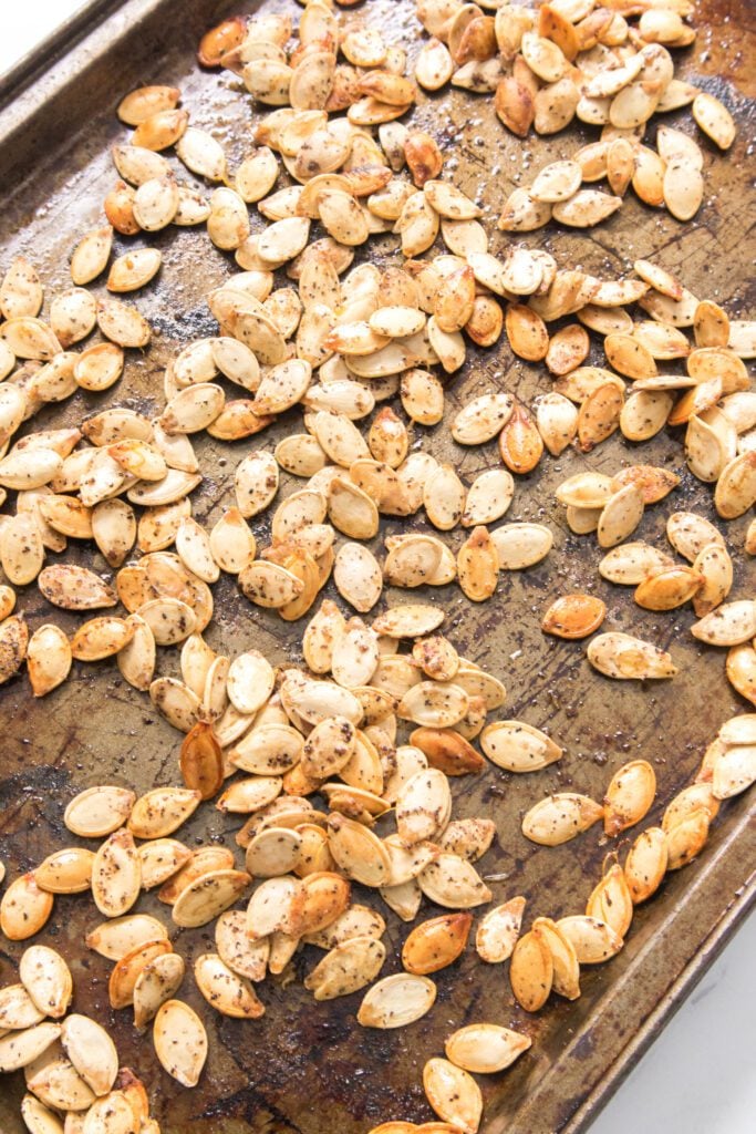 vertical image close up shot of roasted pumpkin seeds on a baking sheet