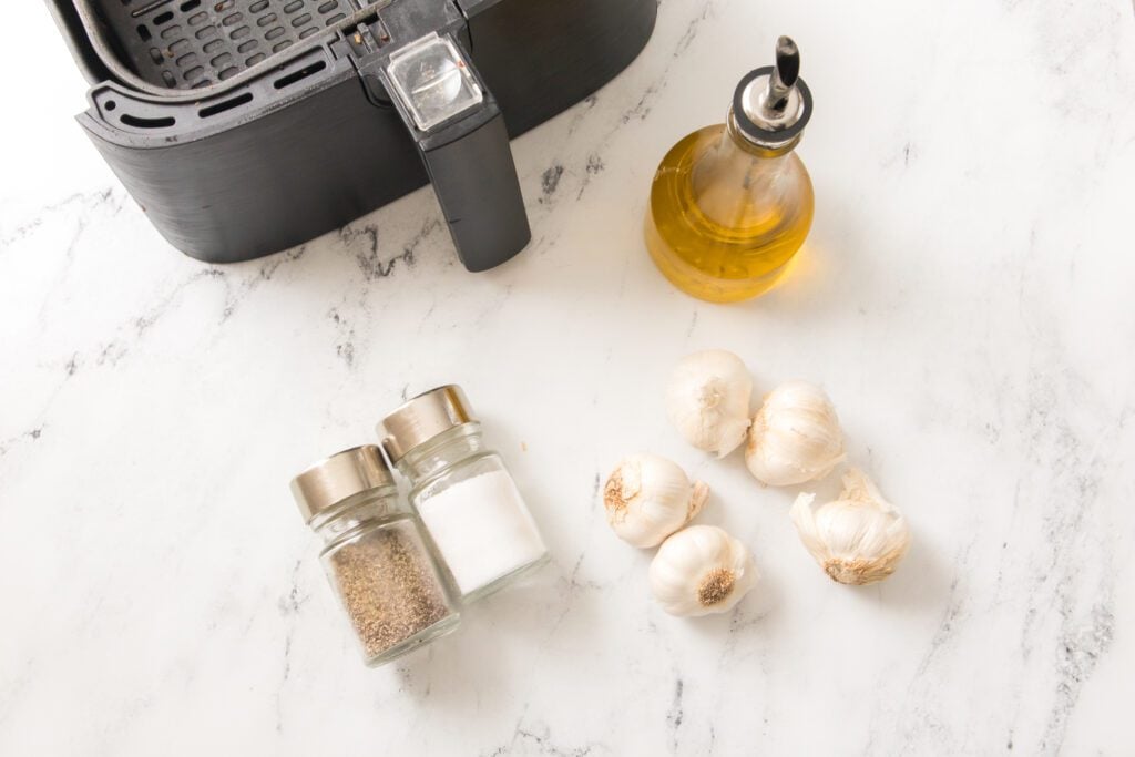 whole garlic, salt, pepper and olive oil with air fryer in background