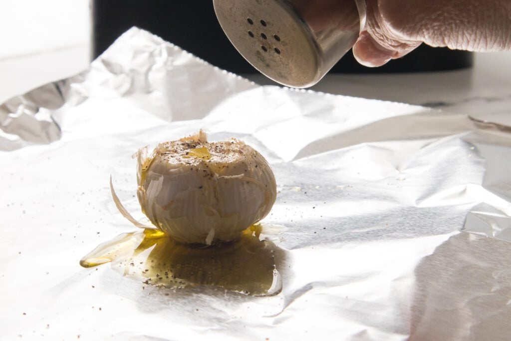 pepper being shaken over garlic on aluminum foil