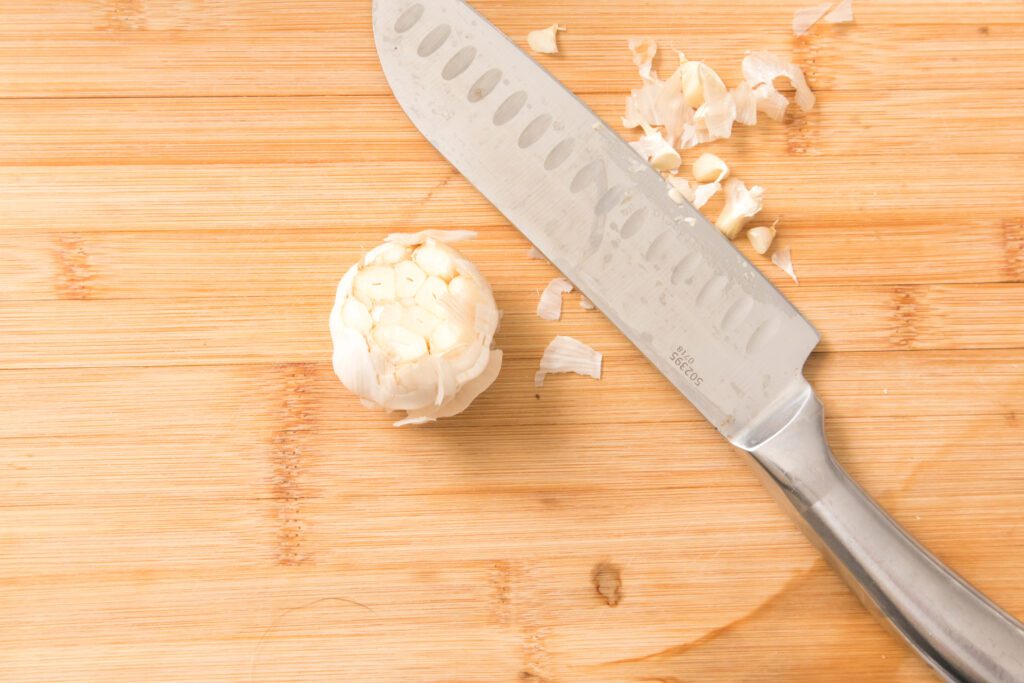 knife on cutting board with top of garlic cut off