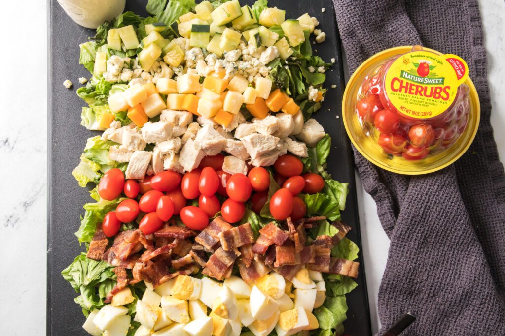 ingredients layered on romaine lettuce, hard boiled eggs, bacon, naturesweet cherub tomatoes, chicken, cheese and cucumbers