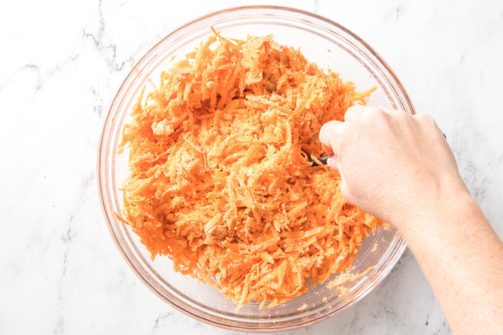 hand mixing sweet potato mixture in a glass bowl