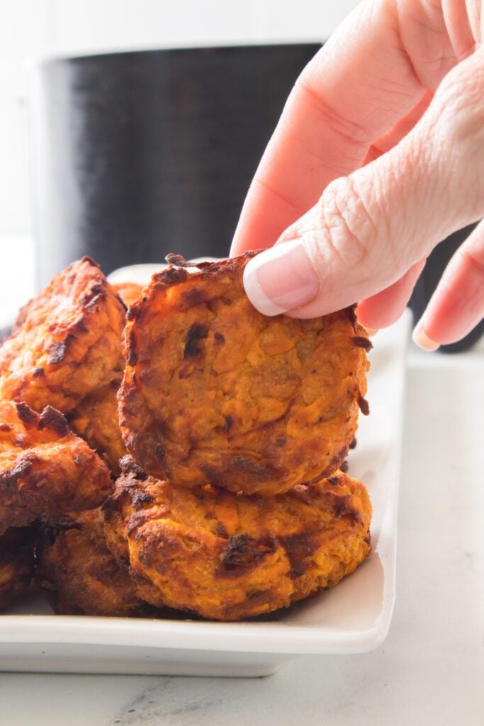 hand holding sweet potato latke with air fryer in background