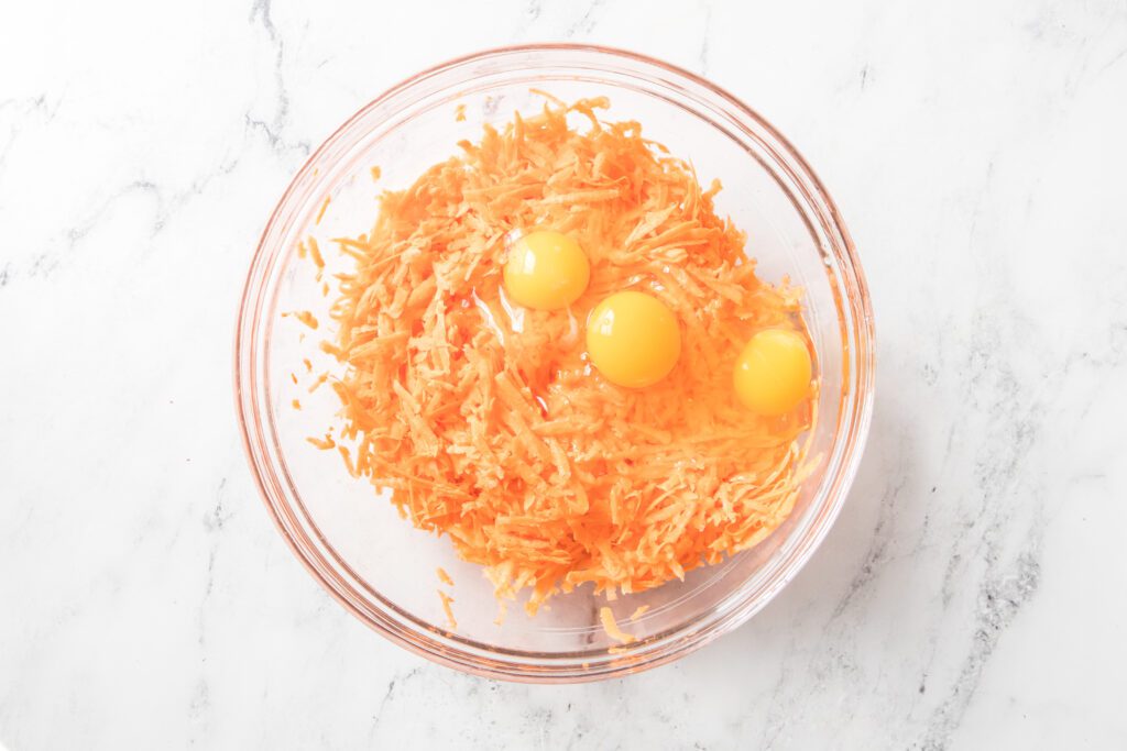 shredded sweet potatoes with 3 eggs in a glass bowl