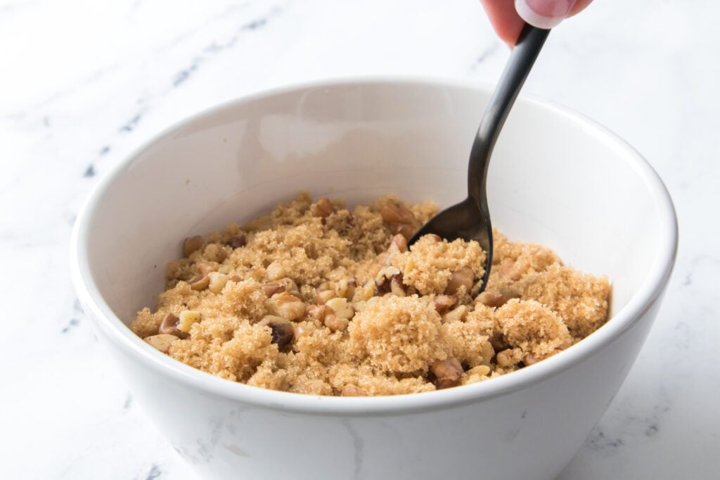 brown sugar and walnuts being mixed with a spoon in a white bowl