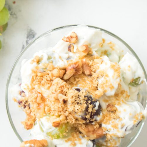 overhead shot of grape salad recipe in a glass bowl topped with brown sugar and walnuts