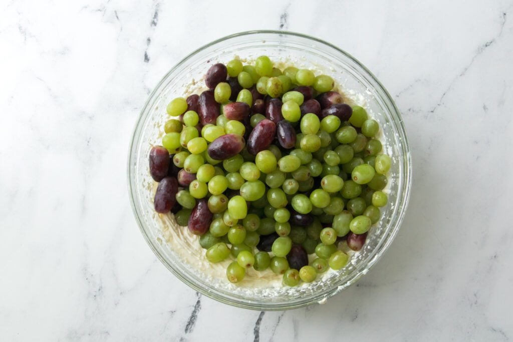 grapes being added to a glass bowl with cream cheese mixture