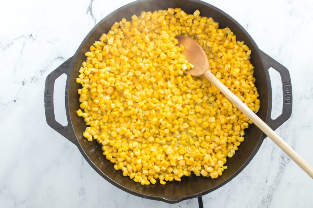 Corn placed in skillet with wooden spoon