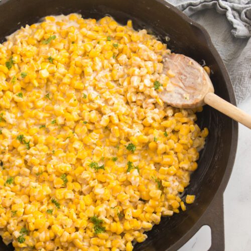 vertical image of honey butter skillet corn recipe in cast iron skillet and wooden spoon