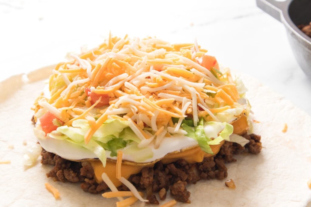 flour tortilla with ground beef, nacho cheese, tostada shell, sour cream, lettuce, tomato and cheese