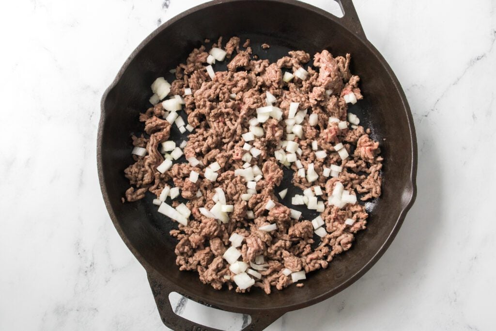 cast iron skillet with brown ground beef and diced onion
