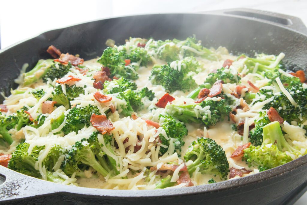 cheese and bacon topped broccoli with garlic sauce in cast iron skillet