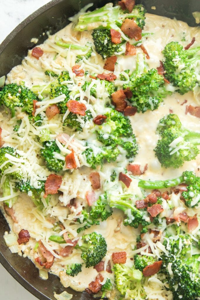 close up vertical shot of broccoli in creamy garlic sauce in cast iron skillet