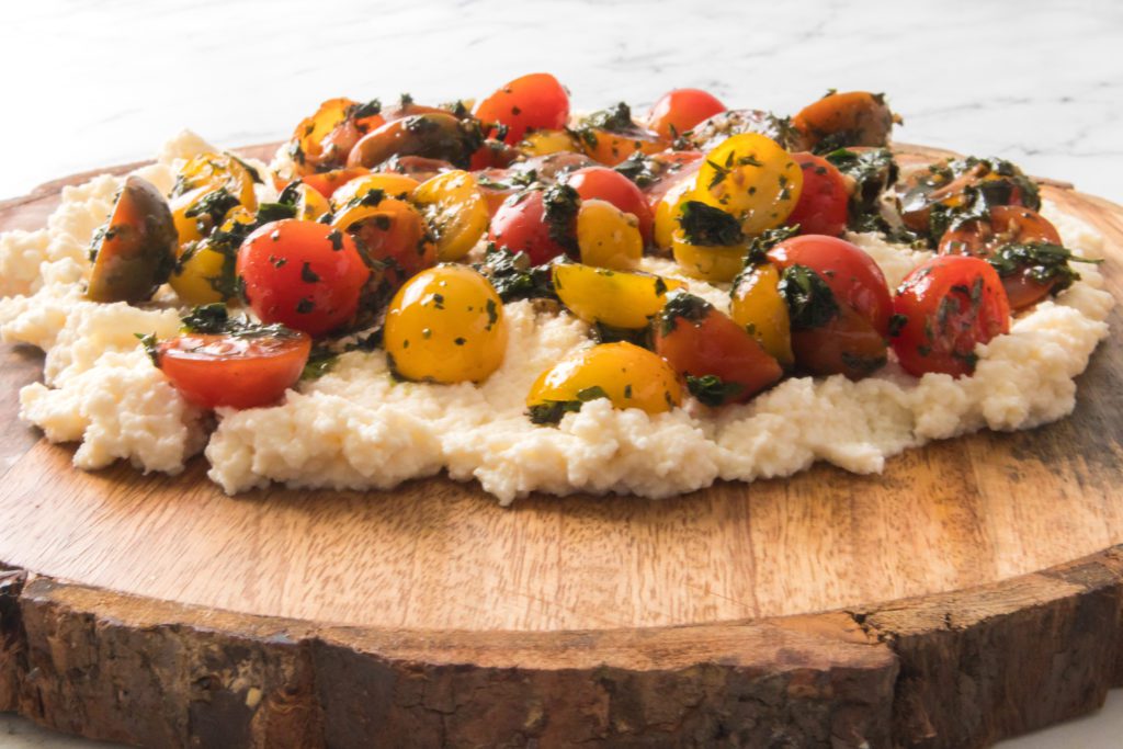 round wooden serving board with ricotta and fresh tomatoes halved with fresh herbs
