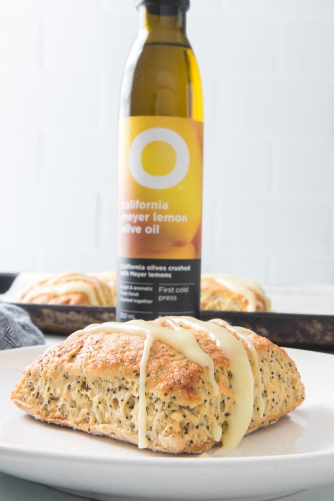vertical close up image of lemon scone with poppy seed and bottle of lemon olive oil in background