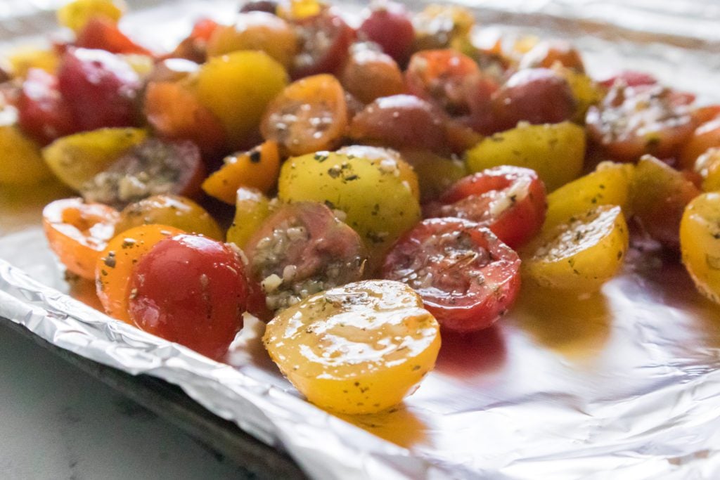 cherry tomatoes on a baking sheet with aluminum foil that have been tossed in olive oil, garlic, Italian seasoning, salt and black pepper