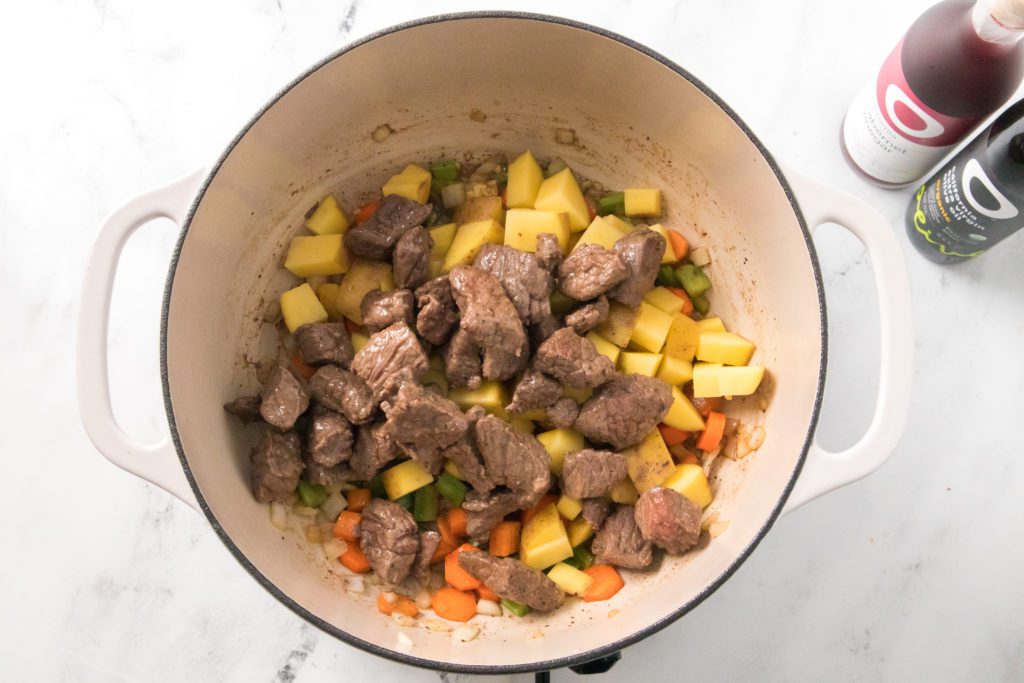 stew meat added to potatoes, carrots, onion, celery and garlic in dutch oven