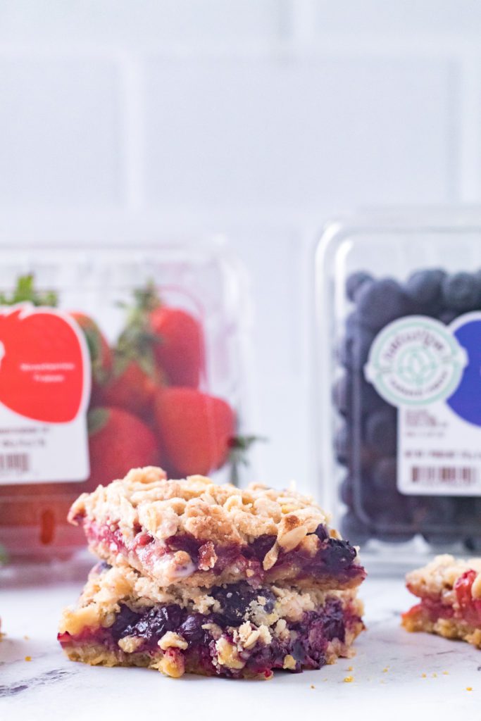 mixed berry crumble bars stack on top of each other with naturipe blueberries and strawberries in background