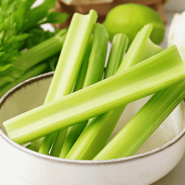 Celery sticks in a bowl with stalks of celery to the side