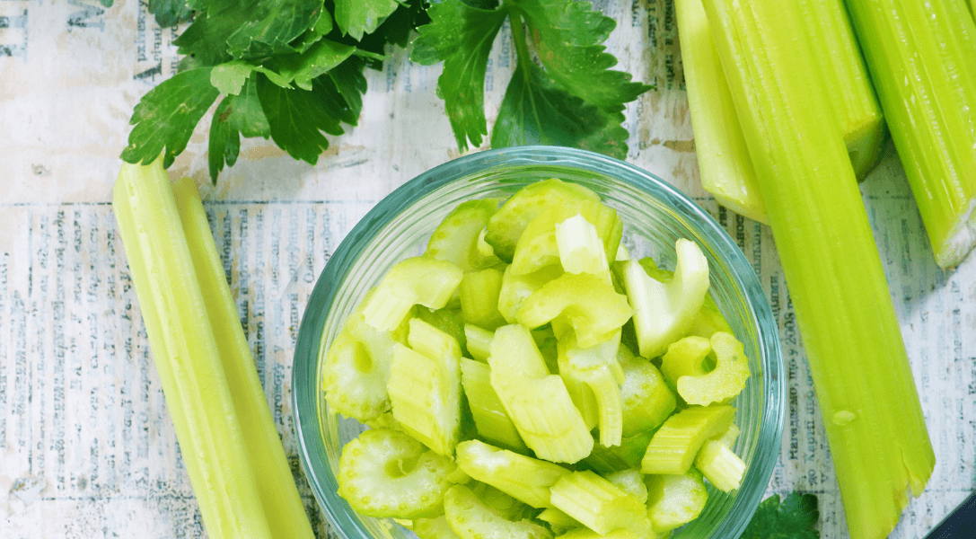 Diced celery in bowl surrounded by celery sticks